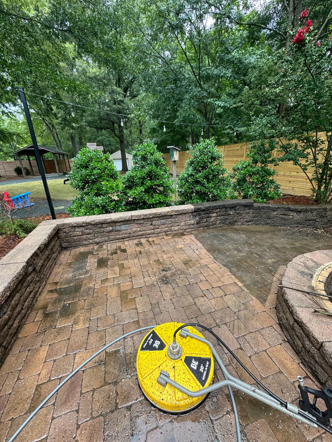 Pressure washer on a stone patio with green bushes and trees in background.