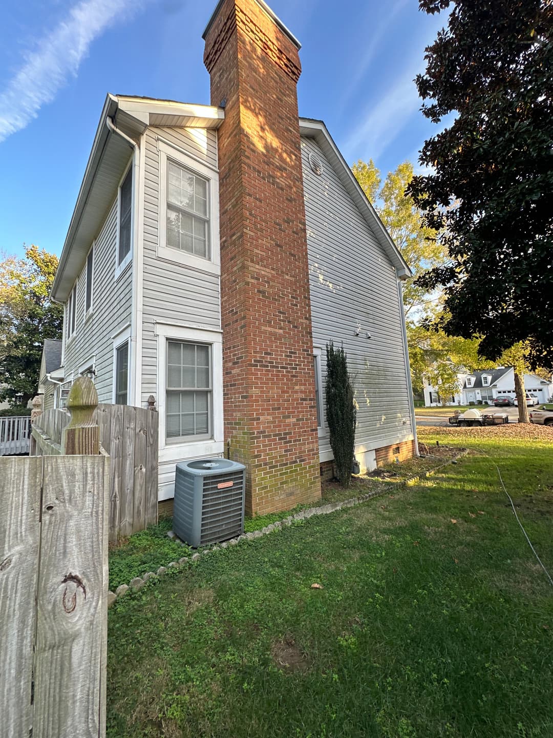 Side view of a residential house with a brick chimney and greenery in the yard.