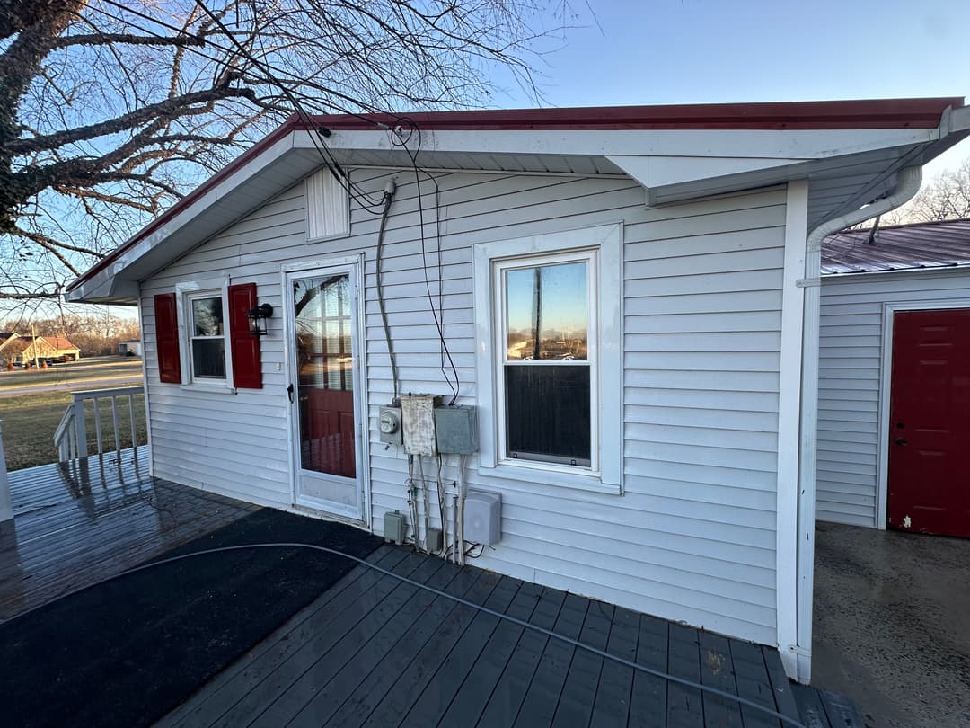 Exterior view of a light blue house with red shutters and a porch, showcasing a clear sky.