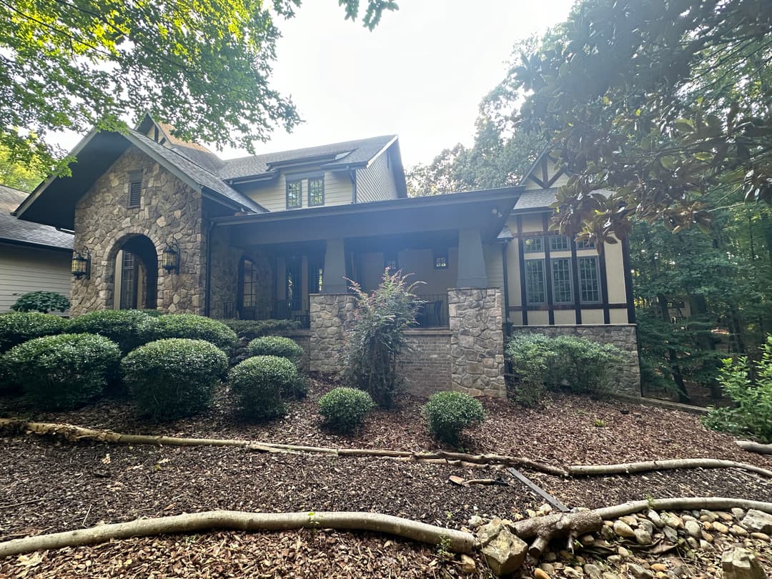 Elegant stone and wood house surrounded by lush greenery and landscaping.