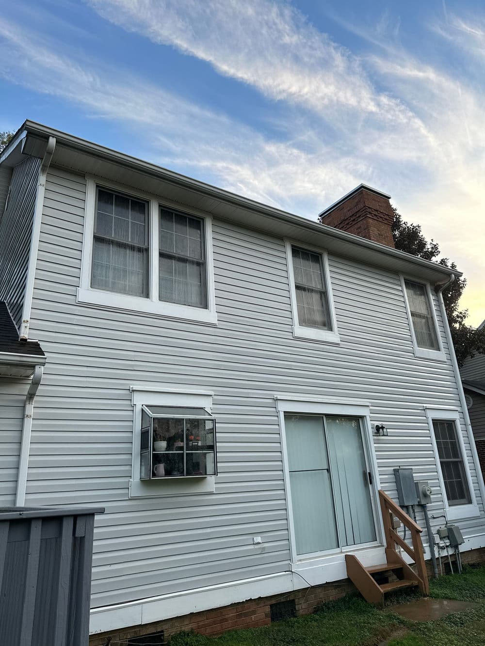 Two-story house with gray siding, windows, and air conditioning unit under a blue sky.