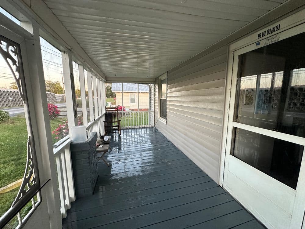 View of a covered porch with a freshly painted floor and a nearby garden.