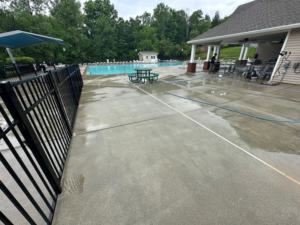 Swimming pool area with wet concrete, picnic tables, and a nearby clubhouse in a lush setting.