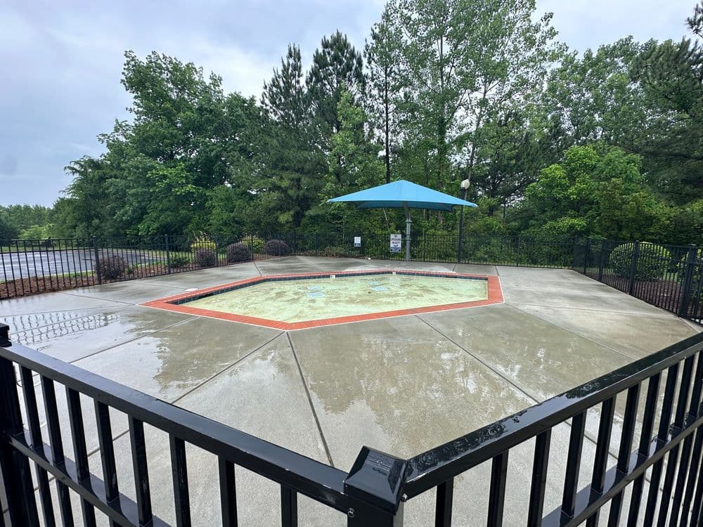 Empty outdoor hot tub under a blue canopy, surrounded by trees and wet pavement.